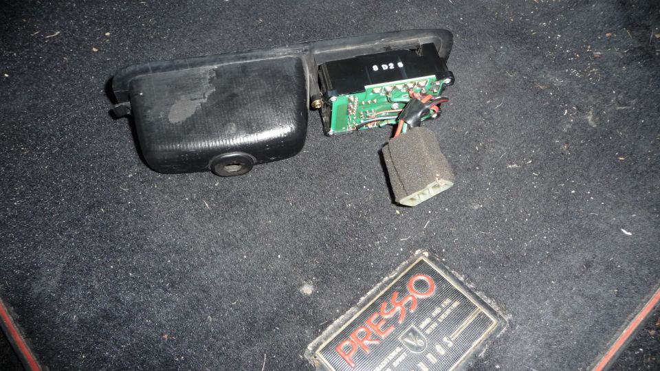 Disassembled car interior component with circuit board and wiring on carpet next to a "PRESSO" emblem.
