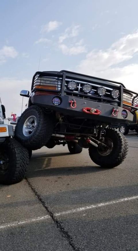 1996 Ford Bronco - A modified Ford Bronco is shown from a low angle, highlighting its large tires and custom front bumper with multiple lights and tow hooks.…