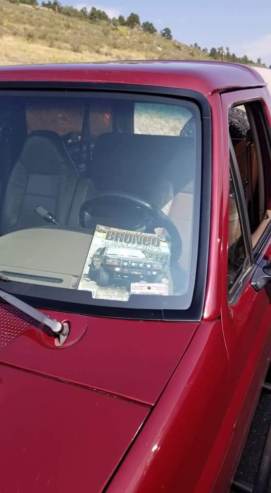 Red Ford Bronco dashboard with a Bronco magazine on it, dry hillside in background.