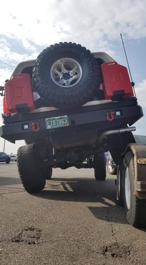 1996 Ford Bronco - The rear view of a lifted off-road vehicle shows a spare tire mounted on the back, two red jerry cans, and a Colorado license plate reading…