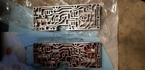 1996 Ford Bronco - Two metal valve bodies are shown, one clean and one with red transmission fluid. They are laid out on a blue shop towel with plastic packag…