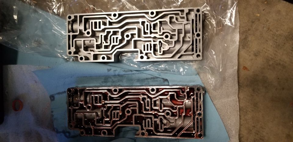 Two metal transmission valve bodies, one clean and one with fluid.
