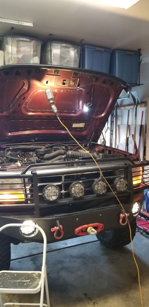 1996 Ford Bronco - The front of a red Ford Bronco is shown with the hood open, revealing the engine bay. The vehicle has a black grille guard with four KC lig…