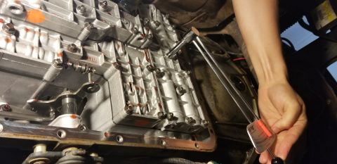 1996 Ford Bronco - A person is using a torque wrench to tighten bolts on the transmission pan of a vehicle. The transmission pan gasket is visible and appears…