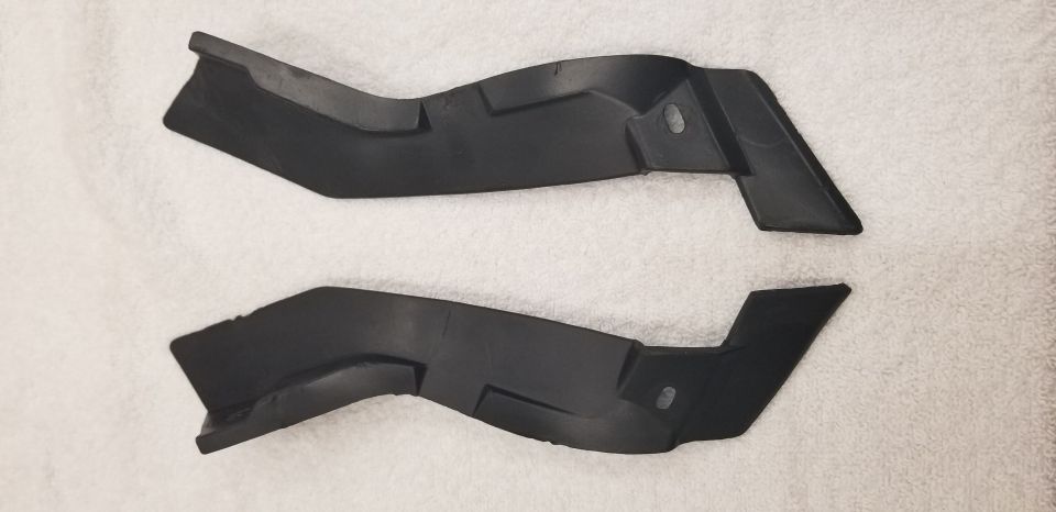Two black plastic automotive trim pieces on a white surface