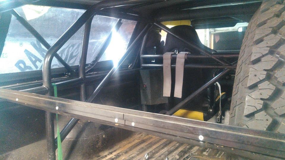 Interior of a custom vehicle with roll cage, racing seat, and spare tire.