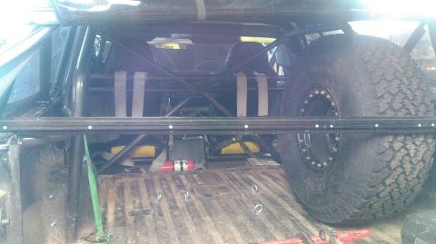 1978 Ford Bronco - The bed of a modified vehicle shows a large spare tire secured with a roll cage and straps. A red fire extinguisher is also visible in the…