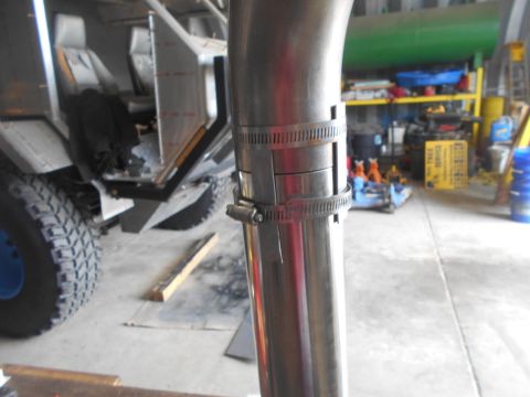 1992 Ford Bronco - A close-up view of a stainless steel exhaust pipe secured with two hose clamps. In the background, the interior of a custom vehicle with se…