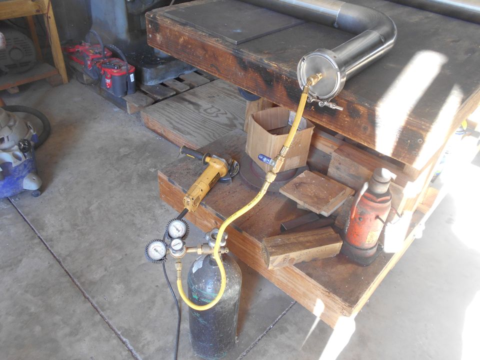 Metal pipe assembly connected to gas cylinder with regulator and gauges, angle grinder, and jack.