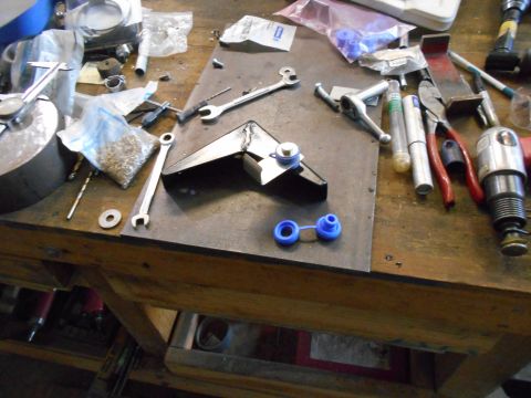 1992 Ford Bronco - A workbench is cluttered with various tools and metal parts, including wrenches, pliers, a drill, and what appears to be a metal bracket wi…