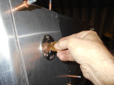 1992 Ford Bronco - A hand inserts a coin into a circular metal port labeled "DIESEL" on a brushed aluminum surface. Copper fittings are visible on the surface.