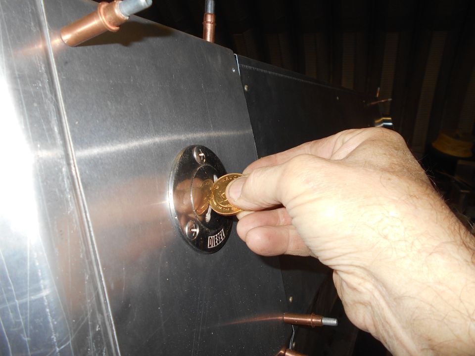 Hand inserting a coin into a DIESEL fuel port on a brushed aluminum surface.