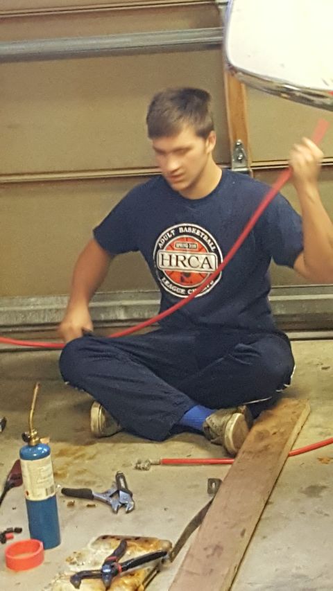 1996 Ford Bronco - A young man sits on the floor in a garage, working with a red hose and a small torch. He is wearing a navy blue t-shirt with a basketball l…