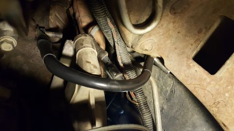 1996 Ford Bronco - A close-up view shows a black hose with silver trim attached to a metal component on a vehicle. The hose curves around other engine parts a…