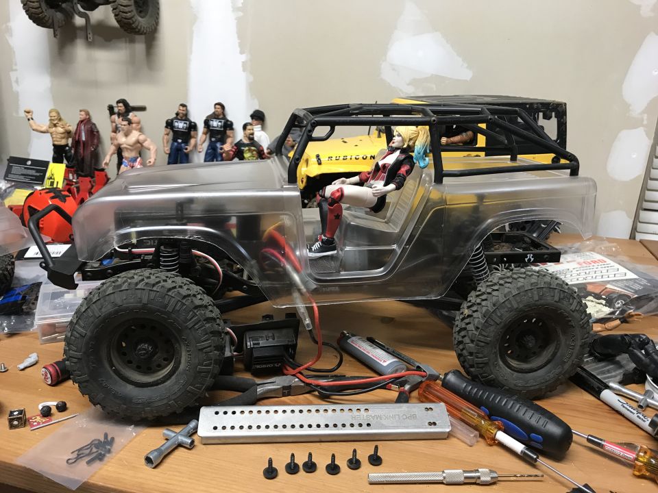 RC car with clear body, Harley Quinn figure, tools, and parts on a workbench.