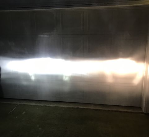 1995 Ford Bronco - The bright headlights of a vehicle are projected onto a garage door, creating a distinct beam pattern. The light is white on the left side…