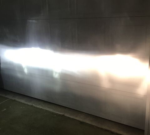 1995 Ford Bronco - The headlights of a vehicle cast a bright, horizontal beam onto a garage door. The light pattern shows a distinct cutoff with a brighter up…