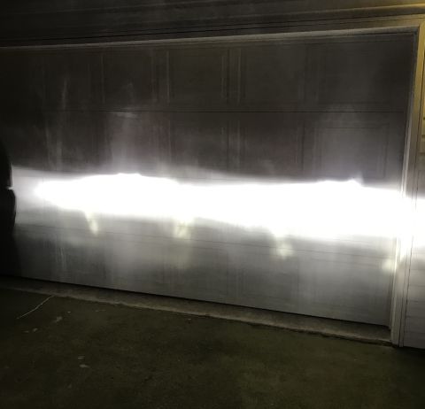 1995 Ford Bronco - The headlights of a vehicle illuminate a garage door, casting a bright beam across the lower half of the door. The garage door is a segment…