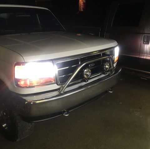 1995 Ford Bronco - The front of a white Ford truck with its headlights on is shown at night. A chrome bull bar with two auxiliary lights is mounted on the fro…