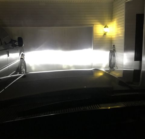 1995 Ford Bronco - The headlights of a dark-colored vehicle illuminate a garage door and a wall-mounted hose reel. A second vehicle, possibly a large SUV or t…