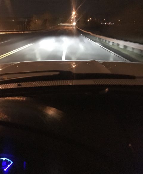 1995 Ford Bronco - View from inside a vehicle at night, looking down a road with bright headlights illuminating the way. The dashboard and windshield are visi…