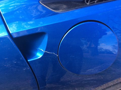 1992 Ford Bronco - A close-up view shows a crack on the blue paint of a vehicle's rear quarter panel, near the fuel filler door. Scratches are visible on the…