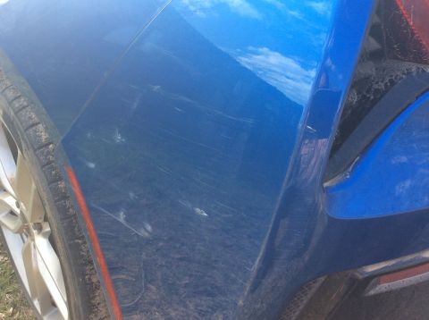 1992 Ford Bronco - A close-up view of the rear passenger side quarter panel of a blue vehicle shows numerous scratches and scuffs. The tire and part of the wh…