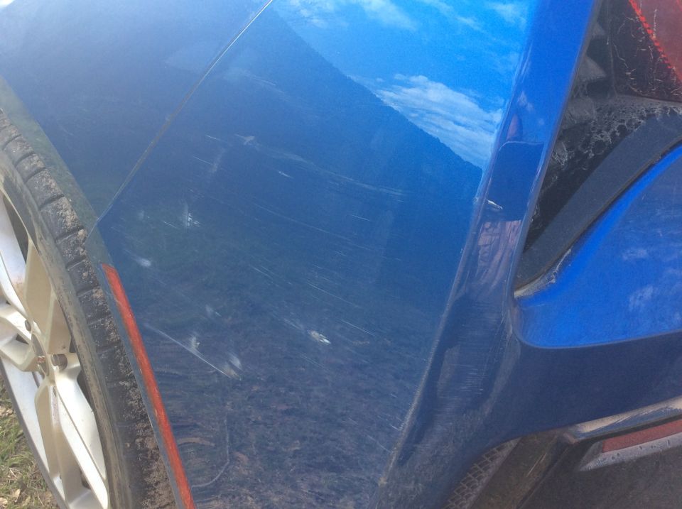 Blue vehicle rear quarter panel with scratches, tire, and red reflector.