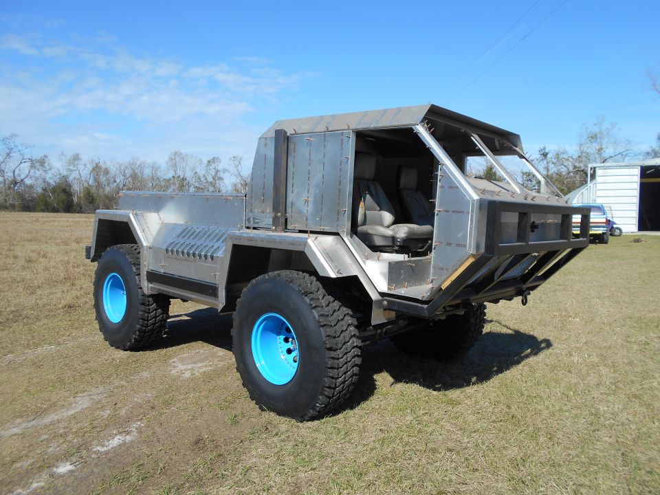 Custom all-metal 4x4 vehicle with blue rims parked on a grassy field.
