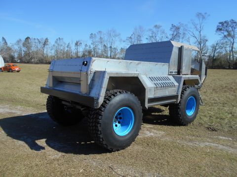 1992 Ford Bronco - A custom-built, six-wheeled vehicle with a metallic gray body and bright blue wheels sits in a grassy field under a clear blue sky. The veh…