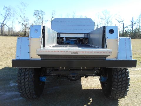 1992 Ford Bronco - Rear view of a custom-built truck bed mounted on a heavy-duty chassis with large off-road tires. The bed is constructed of brushed aluminum…