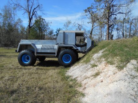 1992 Ford Bronco - A custom-built, silver, four-wheel-drive vehicle with bright blue rims is parked on a grassy incline. The vehicle has a utilitarian, angula…
