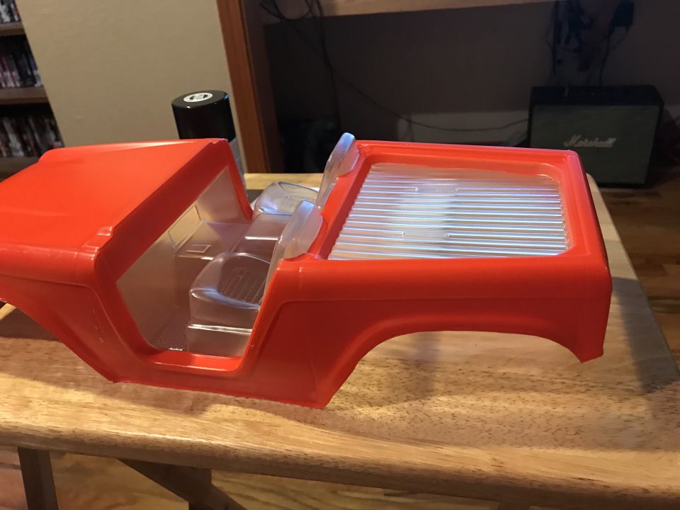 Red plastic RC car body with clear interior seats and bed, on a wooden table.