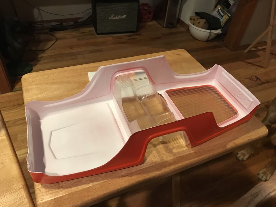 Red and white RC car body shell with clear interior parts on a wooden table.