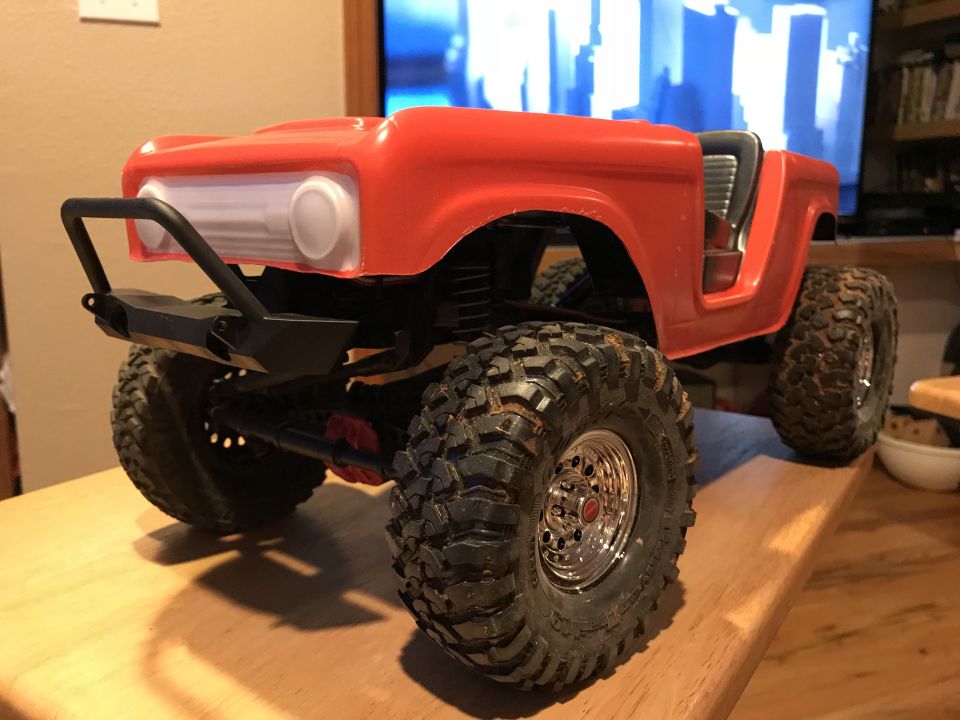 Orange RC rock crawler with black bumper and large tires on a wooden surface.
