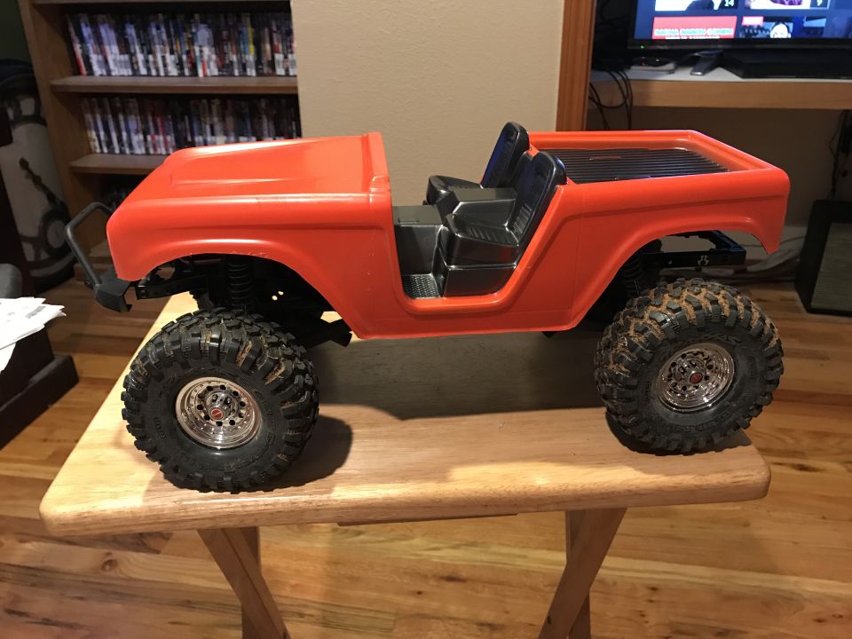 Orange RC Bronco body with black interior and off-road tires on a wooden table.