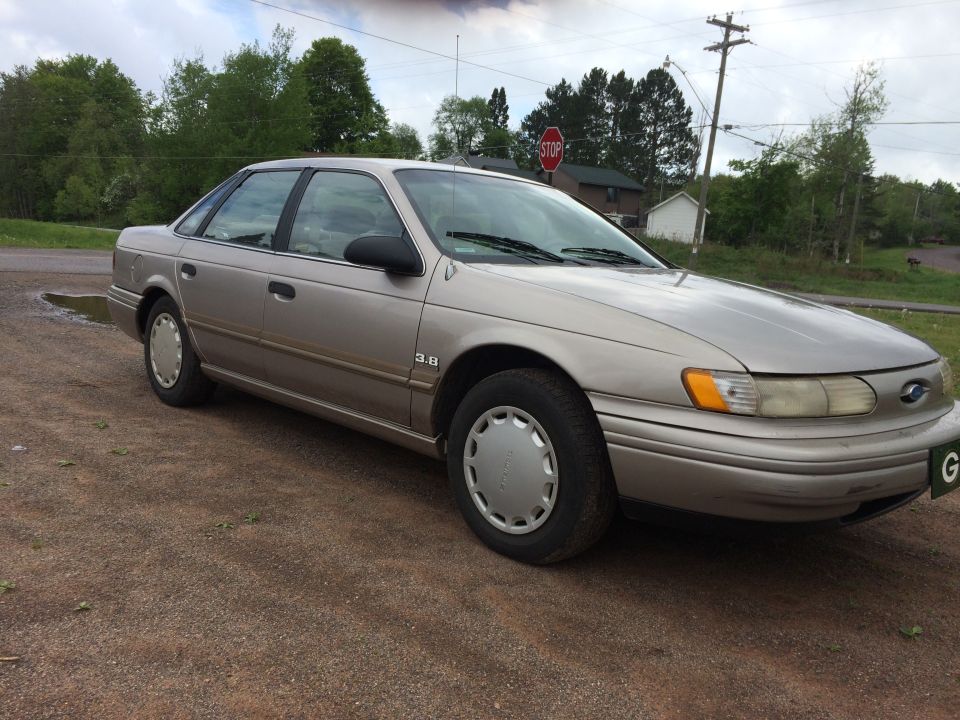 1995 Ford Taurus sedan, tan color, parked on gravel.