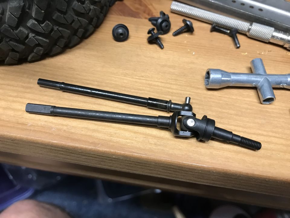 Two black metal drive shafts with universal joints on a wooden surface.