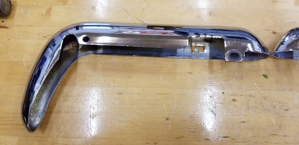 Chrome bumper part with cutouts and holes on a wooden surface