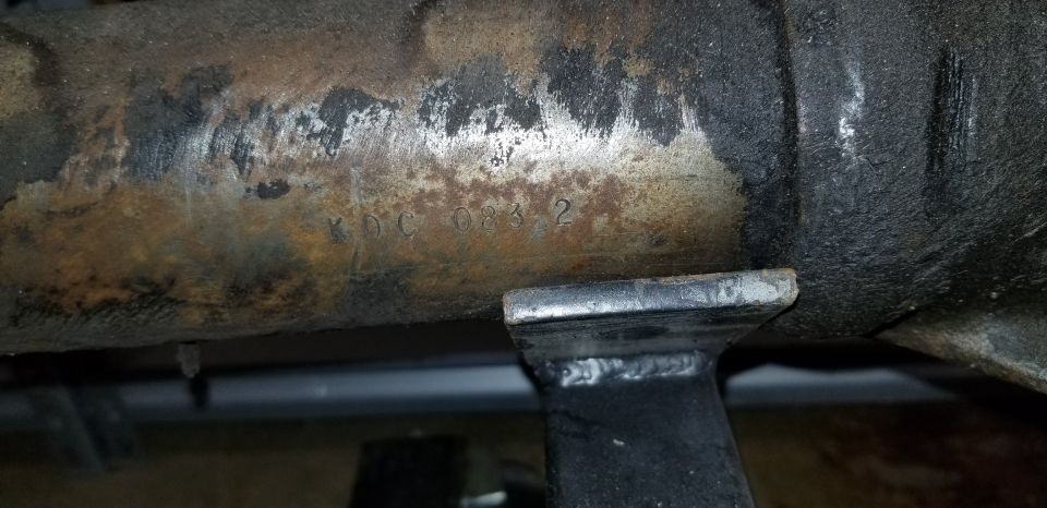 Stamped text KDC 083 2 on a rusty metal axle.