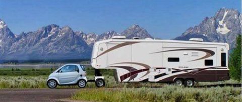 1992 Ford Bronco - A white Smart car tows a large fifth-wheel RV down a road with a mountainous backdrop.