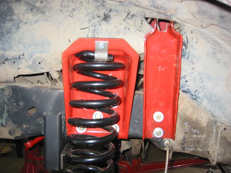Black coil spring in red bracket on vehicle underside suspension
