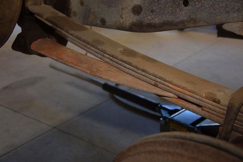 1996 Ford Bronco - A close-up view shows the rusty leaf springs of a vehicle, supported by a jack underneath. The suspension components are weathered and show…