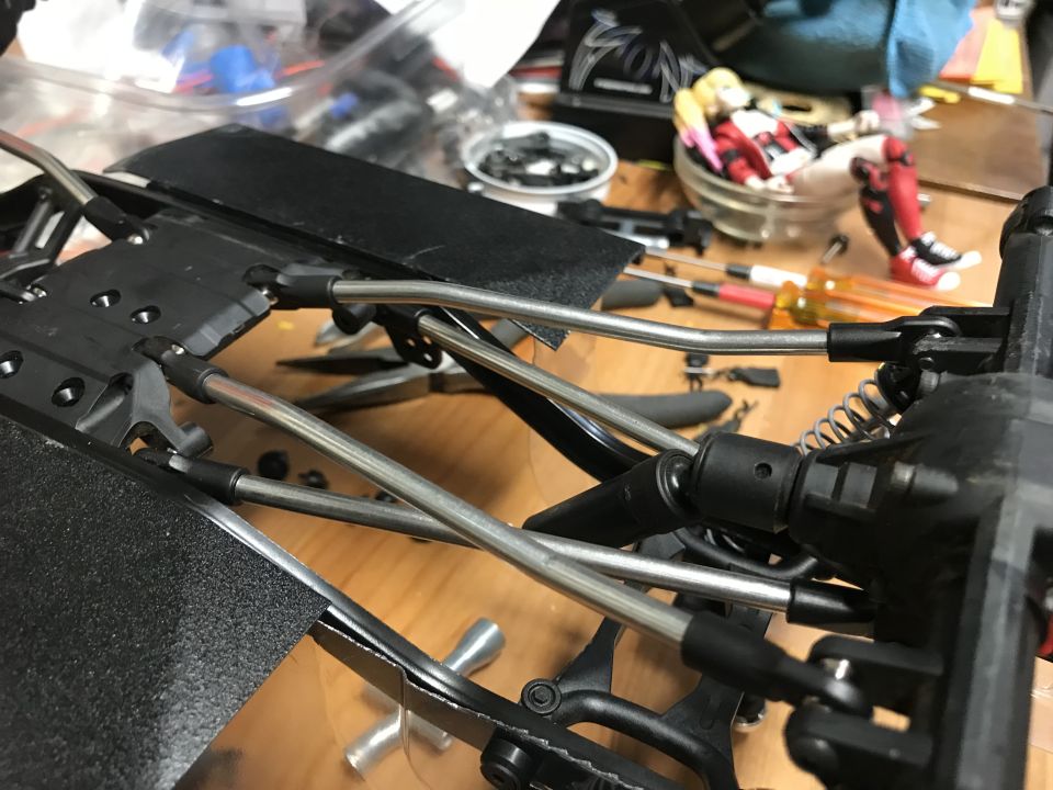 RC car chassis and suspension with tools and figures in background.