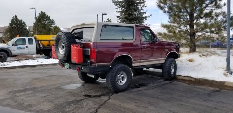 1996 Ford Bronco - The rear passenger side of a lifted, maroon 1996 Ford Bronco is shown parked on asphalt with patches of snow. It features a spare tire moun…