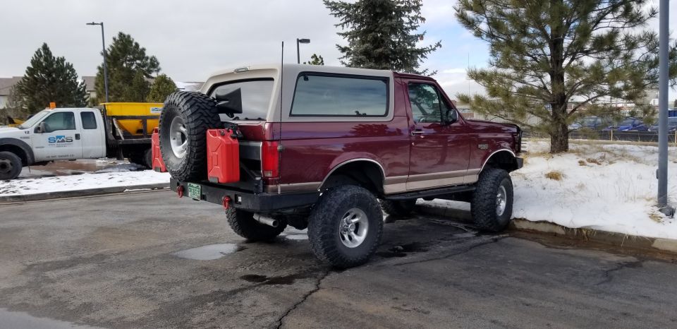 Lifted maroon 1996 Ford Bronco rear passenger side view with spare tire and jerry cans.