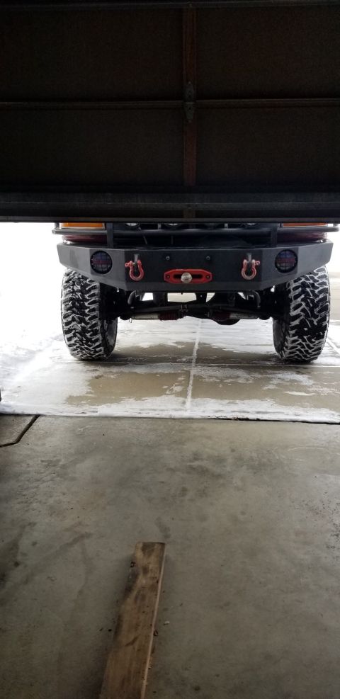 1996 Ford Bronco - The rear of a modified off-road vehicle is shown parked in a garage with snow on the ground. Visible modifications include a heavy-duty bum…