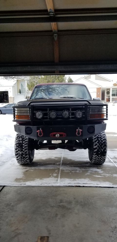 1996 Ford Bronco - A black 1996 Ford Bronco is parked in a garage with a snow-covered driveway and houses visible in the background. The truck features a cust…