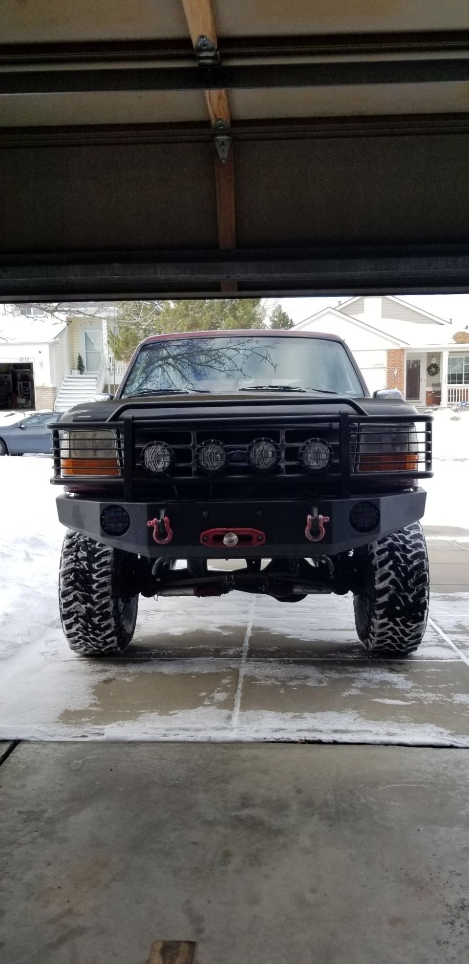 Black 1996 Ford Bronco with custom bumper and KC lights, parked in a snowy driveway.