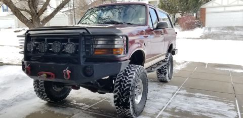 1996 Ford Bronco - A lifted, maroon 1996 Ford Bronco with a custom front bumper and KC lights sits in a snowy driveway. The vehicle is equipped with large, ag…